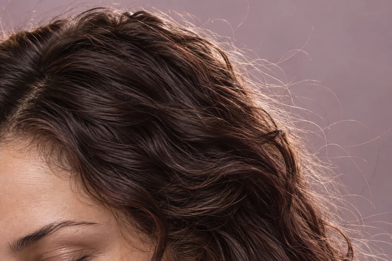 Close-up of fine flyaway strands extending beyond dark wavy hair against a lavender background