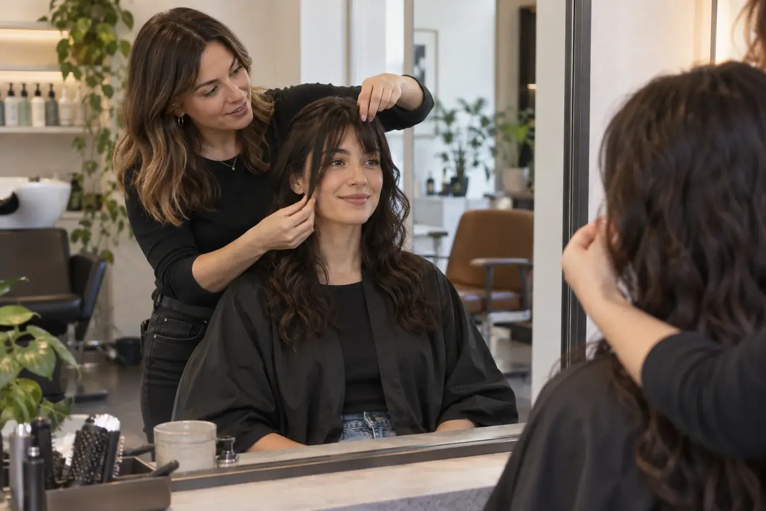 Stylist compares shorter and longer fringe sections on a client in a salon mirror